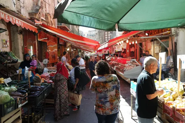 A market lane under coloured awnings with vegetable stalls and shoppers