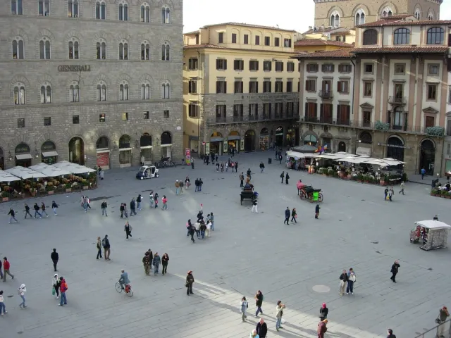A wide paved square with strollers ringed by stone palaces