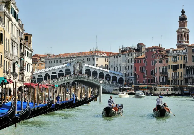 An arched stone bridge over a wide canal with gondolas and coloured houses