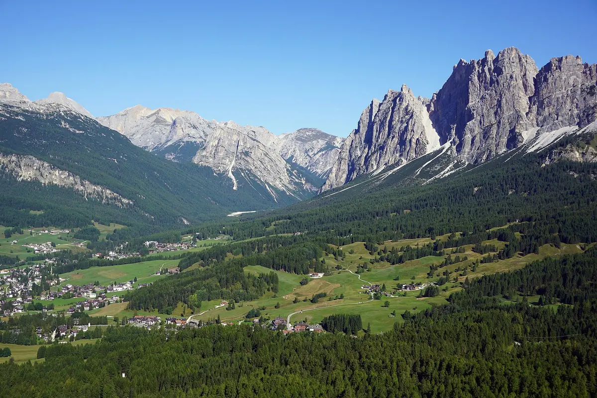 A wide green valley with a scattered town, ringed by spruce forest and jagged rock peaks