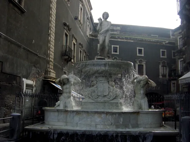 A stone fountain with an elephant statue and obelisk in a city square