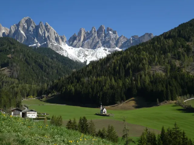 A small steepled chapel in a green meadow below rock spires