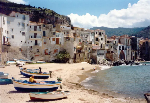 A narrow sandy beach with boats and old houses coming down to the water