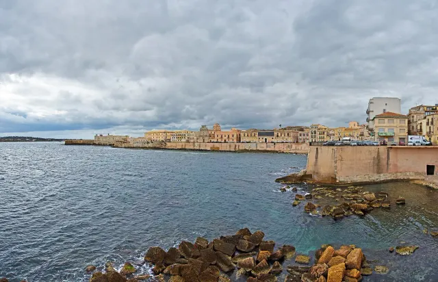 A pale stone seafront with a low wall and blue water