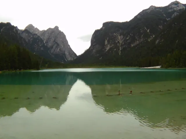 A calm green lake between forested slopes and grey mountains