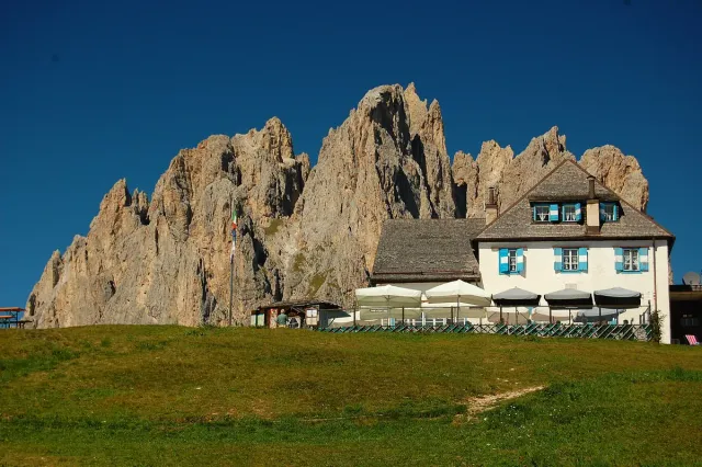 A mountain hut on a grassy shelf below tall rock towers