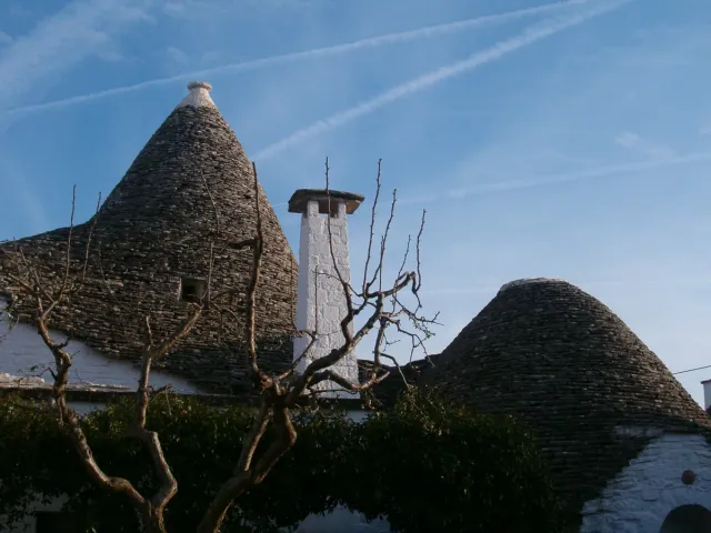 Conical stone roofs beneath a whitewashed chimney against a blue sky