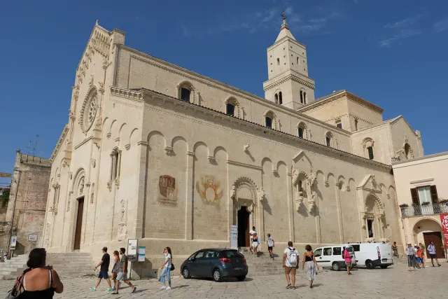A pale stone cathedral front with a rose window and a tall bell tower