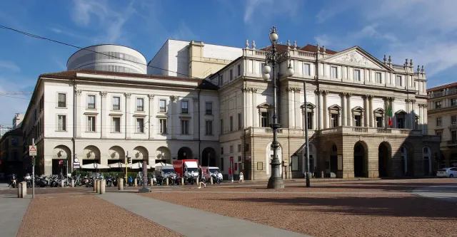 A pale neoclassical opera house on a square with passers by