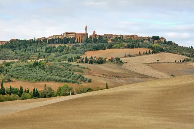 A stone town on a ridge above ploughed fields and olive trees