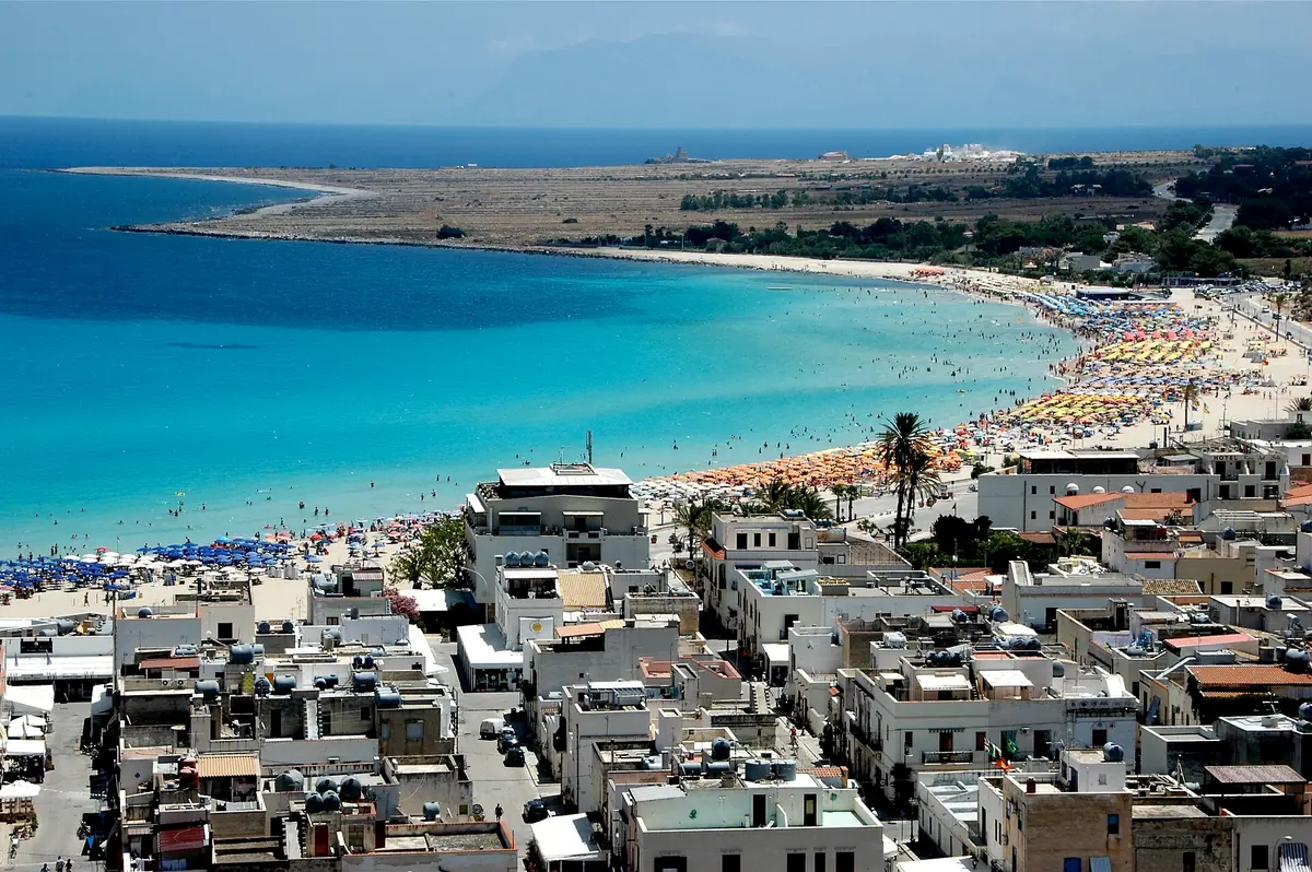 A turquoise bay with a beach strip full of parasols and white rooftops in the foreground