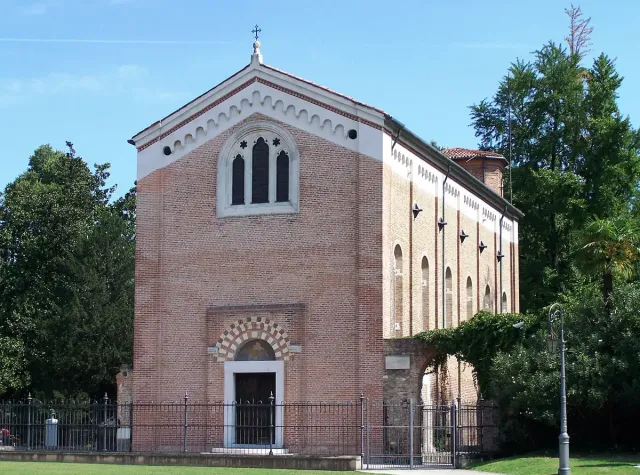 A small red brick chapel with arched windows in a garden