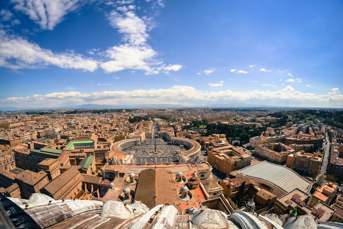 High view over an elliptical square ringed by a colonnade and city rooftops to the horizon