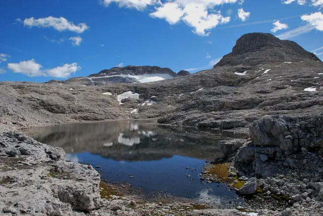 A clear mountain lake between rocky slopes and patches of snow