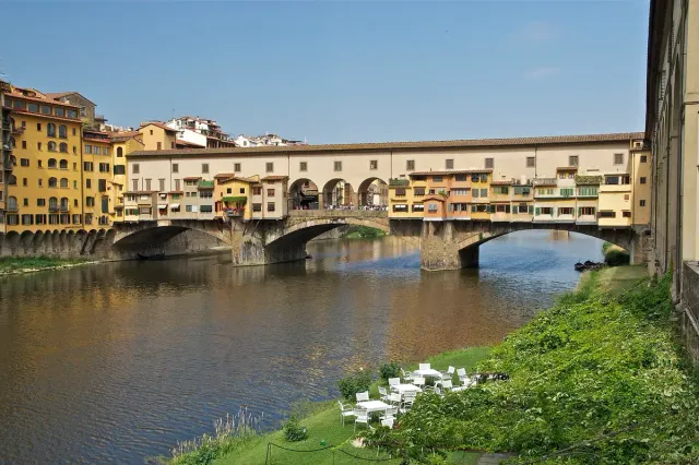 A stone bridge lined with overhanging coloured houses above a green river