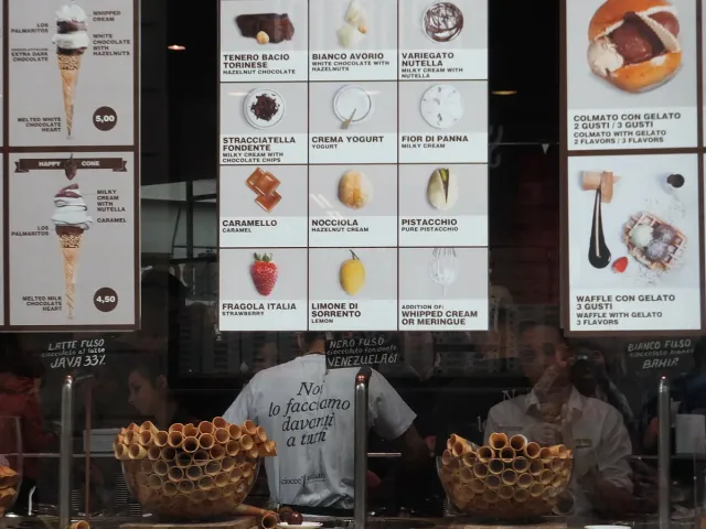 A gelato counter with lit menu boards and stacked cones