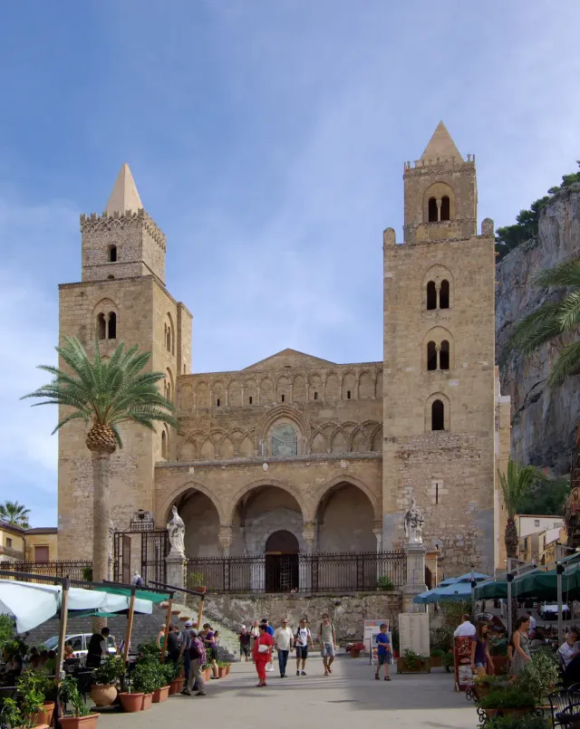A Norman cathedral with two square towers below a rock cliff