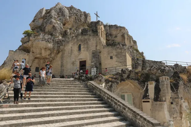 A church carved into rock with stone steps and visitors climbing to it