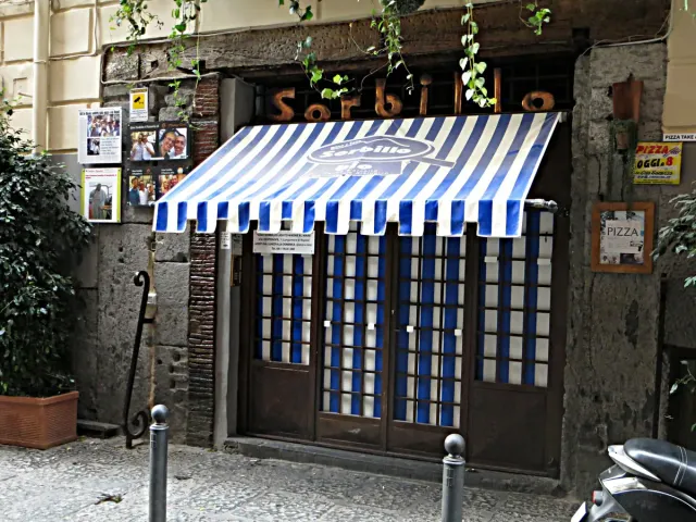 A pizzeria front with a blue and white striped awning on a narrow lane