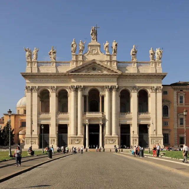 A pale classical facade with columns and giant statues along the roofline