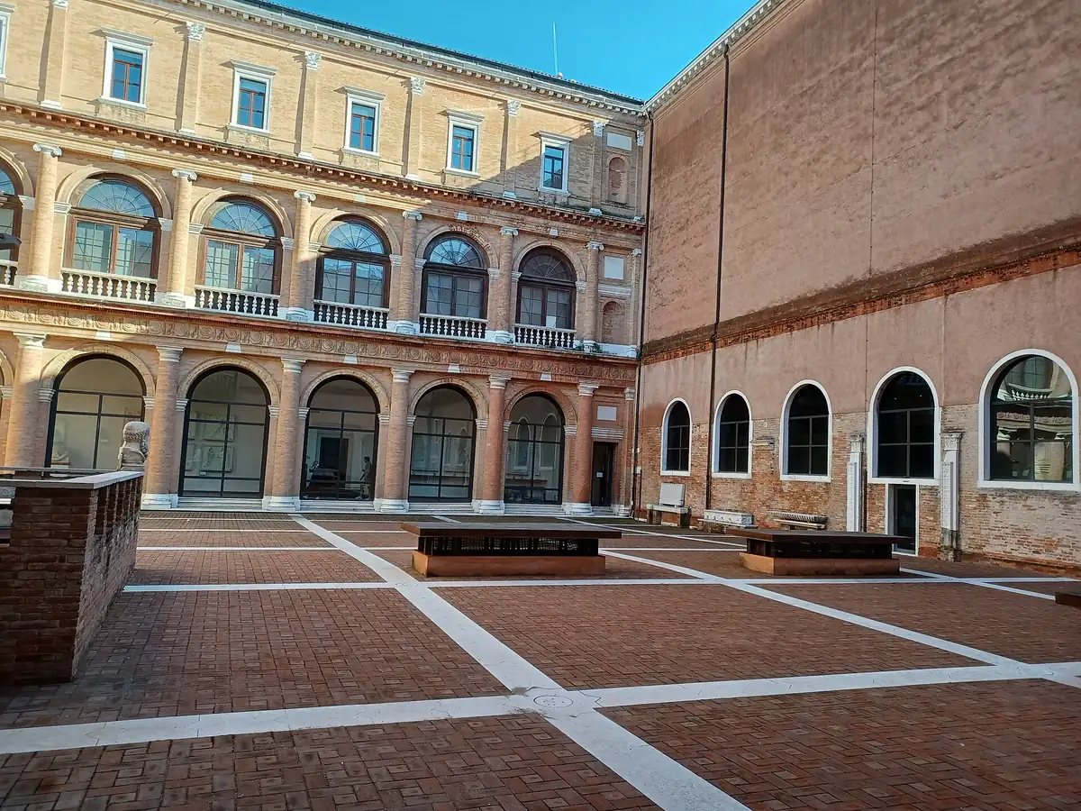 A wide brick courtyard with two tiers of stone arcades and arched windows