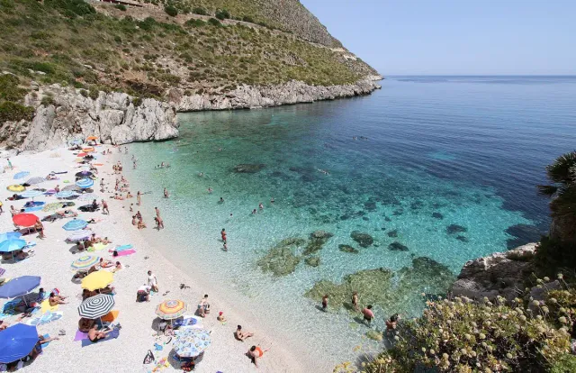 A small pebble cove with turquoise water and parasols between cliffs