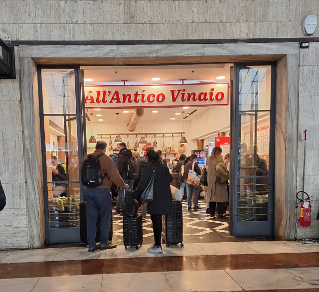 A small sandwich shop with a red sign and a queue at the door