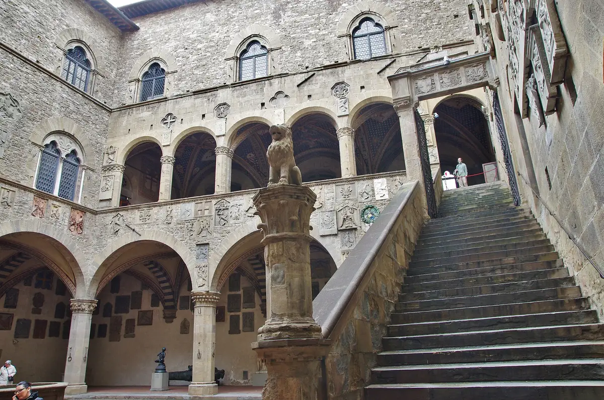 A stone courtyard with a broad staircase, an arcaded loggia and coats of arms on the walls