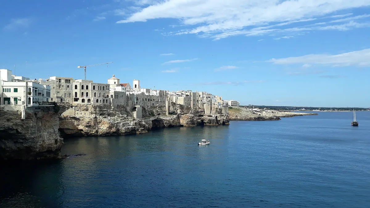White houses on the edge of a limestone cliff above a blue sea under a bright sky