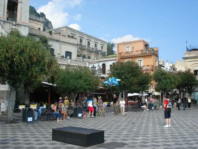 A black and white paved square with visitors, cafes and a balustrade over the sea