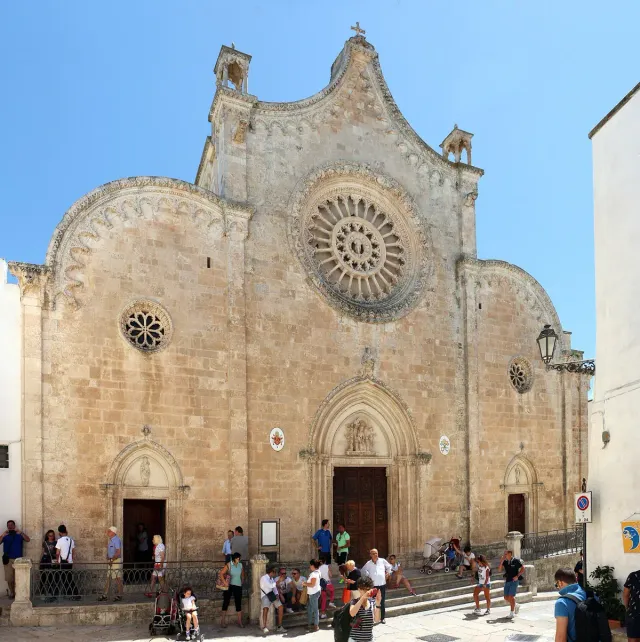 A pale stone cathedral front with a large rose window and three portals
