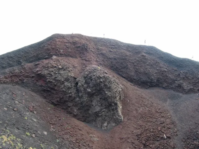A rust coloured volcanic crater slope scattered with black rock