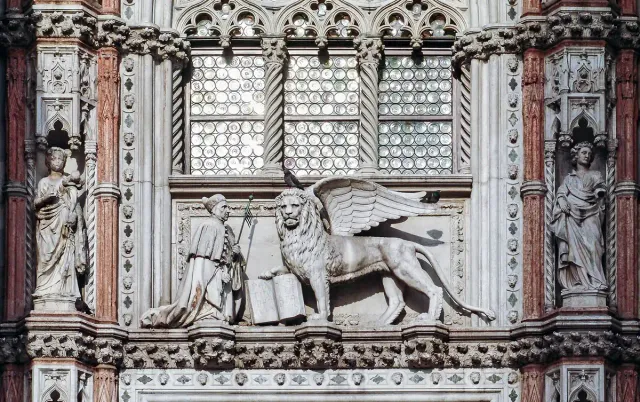 A carved Gothic stone gateway with a winged lion relief and statues