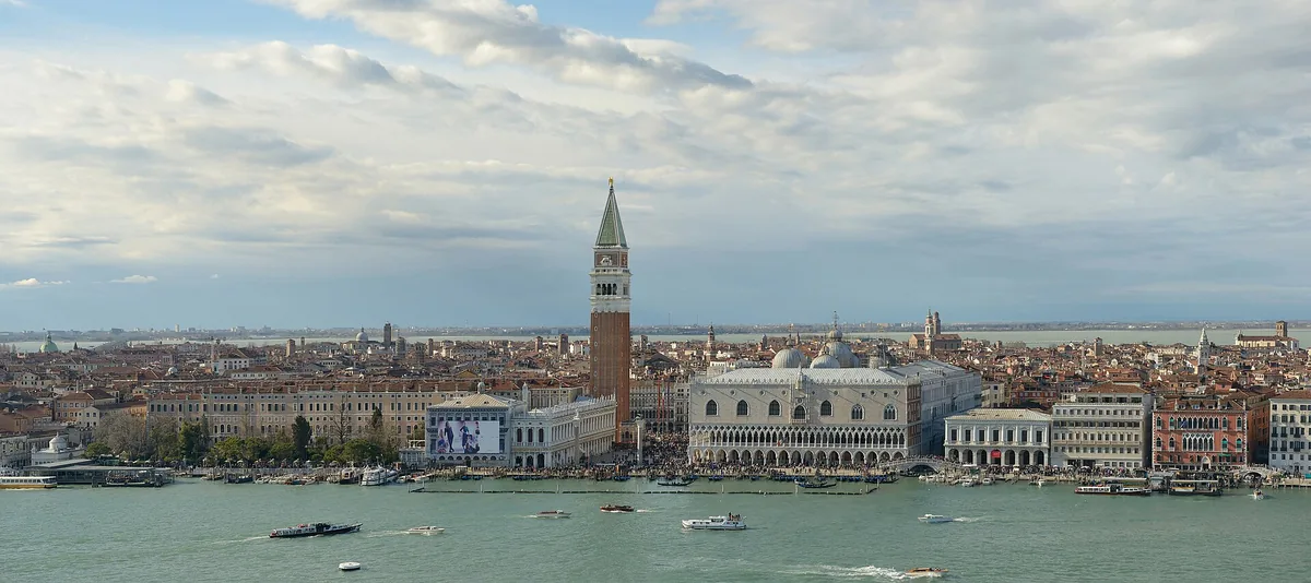 A view from the water of a tall brick bell tower and a Gothic palace in white and pink marble