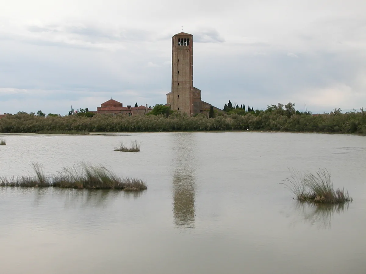 A brick bell tower on an island across a lagoon marsh, reflected in still water