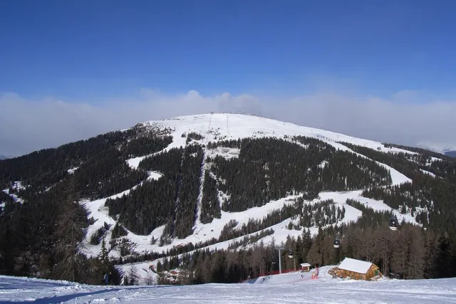 A snowy mountain with wide ski runs and forest at its base