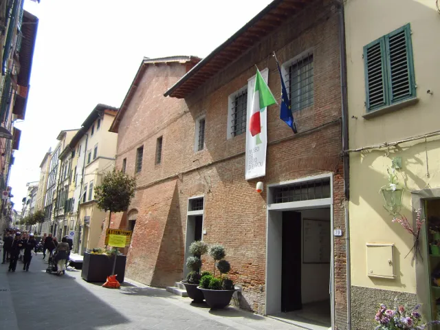 A sand coloured museum building with flags at the entrance on a quiet street