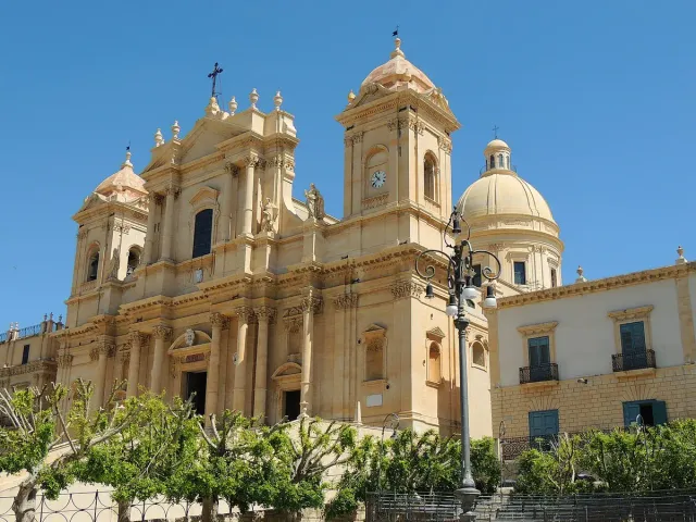 A golden stone baroque cathedral with twin towers above a broad stair