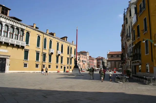 A long Venetian square with mustard coloured houses and green shutters