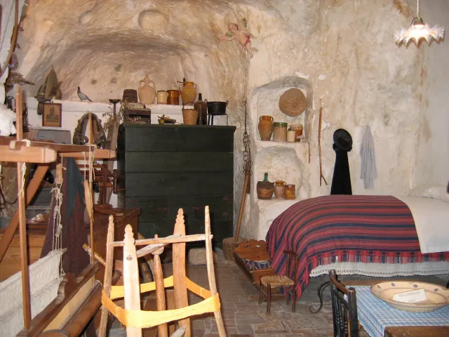 A rock cut room with a striped bed cover and old household tools