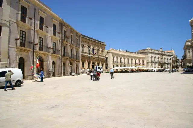 A wide square paved in white stone with pale baroque facades