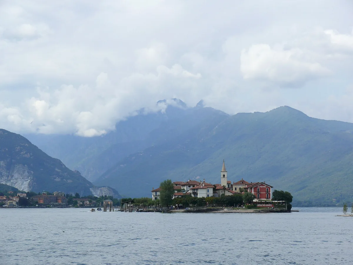 A small island of fishermen's houses and a bell tower in the middle of a lake, mountains behind