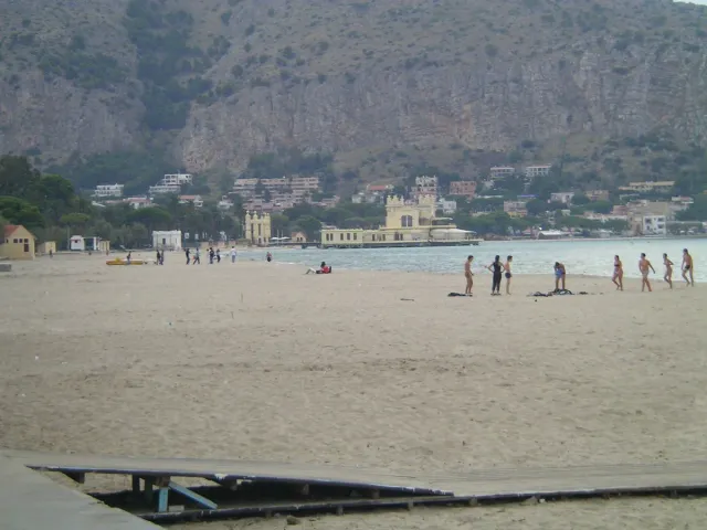 A wide sandy beach with bathers and shallow water below a mountain