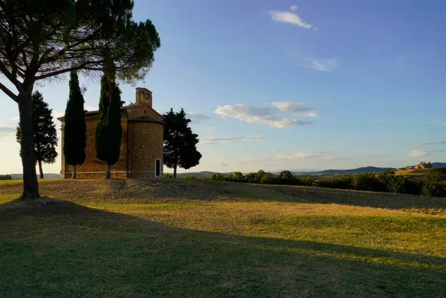 A small stone chapel among cypresses on a hill in warm evening light