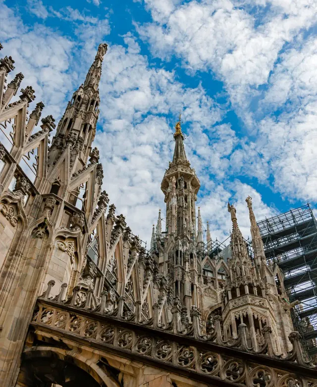 Pointed Gothic marble spires topped with statues against a blue sky