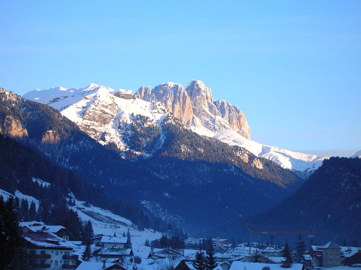 Sunlit snowy Dolomite peaks above a shaded wooded valley