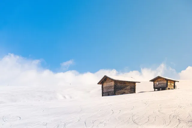 A white snowy plateau with two lone wooden huts under a blue sky