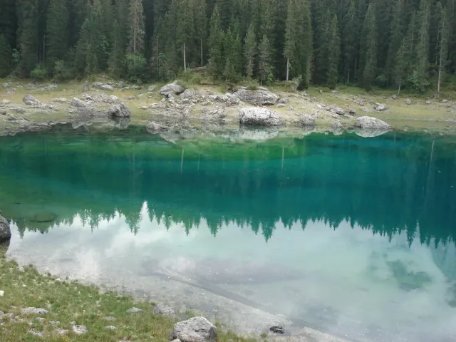 A clear green lake reflecting spruce forest and rock