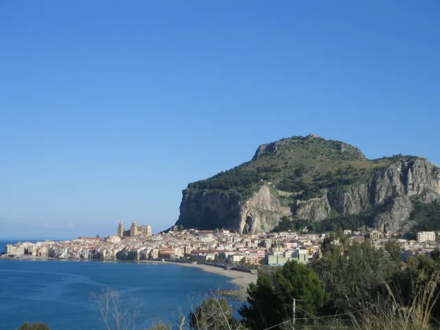 A huge rock crag above a coastal town of tiled roofs and blue sea