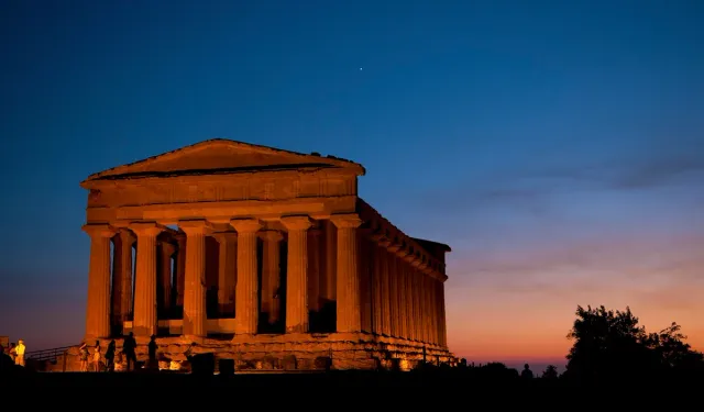 A Greek temple lit warm against a sunset sky